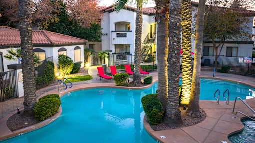 A pool surrounded by palm trees and red chairs.