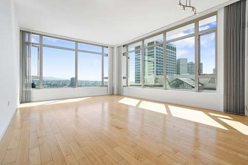 A room with wooden floors and large windows overlooking a cityscape at The Grand Apartments, Oakland 94612