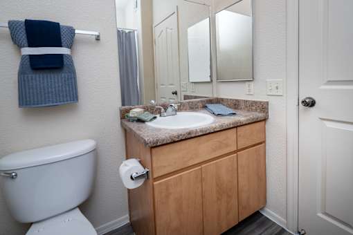 A bathroom with a white toilet, wooden cabinets, and a blue towel hanging on the wall.