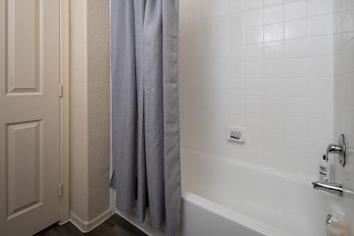 A white tiled bathroom with a grey shower curtain.