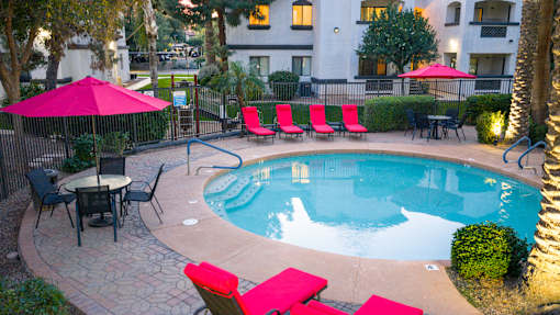 A pool surrounded by red chairs and umbrellas.