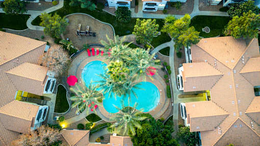 A large swimming pool surrounded by palm trees and a fountain in the middle of a housing complex.
