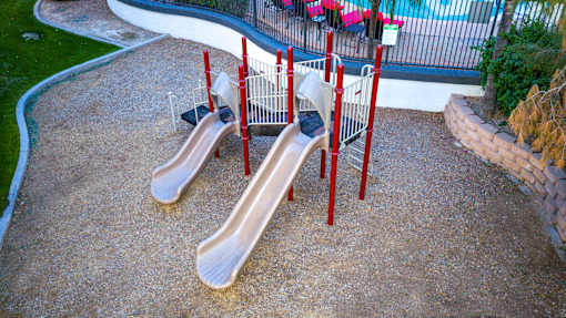 Two slides in a playground with red poles.