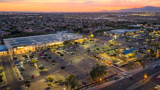 A parking lot with cars and a shopping center in the background during sunset.
