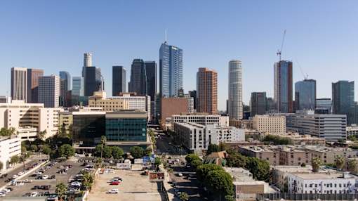 A cityscape with a mix of modern and older buildings, a parking lot in the foreground, and a clear blue sky at Wilshire Valencia Apartment, California