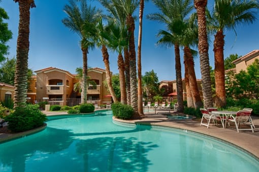 Apartments for Rent in Surprise, AZ - The Village at West Point - Sparkling Lagoon-Style Swimming Pool with Palm Trees, Tables, and Chairs.