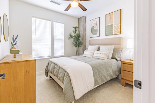 Bedroom with Carpeted Flooring, Bed, Nightstand with Lamp, Dresser, Framed Circular Mirror, Ceiling Fan, Wall Art, and Windows at Waterford RiNo, Denver, Colorado