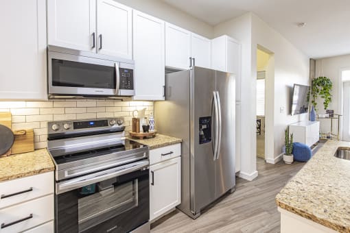 Modern Kitchen with Wood-Style Plank Flooring, Stainless Steel Appliances, Granite Countertops, Subway Tile Backsplash, and White Shaker Cabinetry at Waterford RiNo, Denver, Colorado