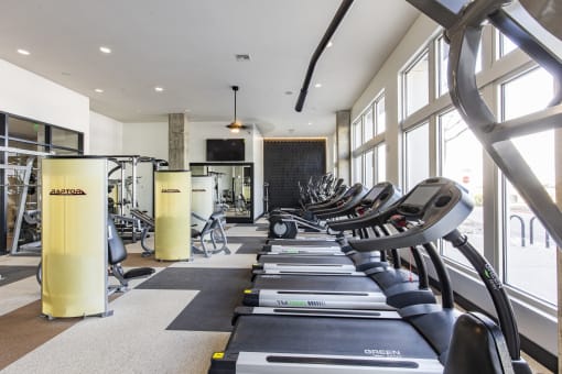 a row of treadmills in a gym with large windows at Waterford RiNo, Denver, CO 80216