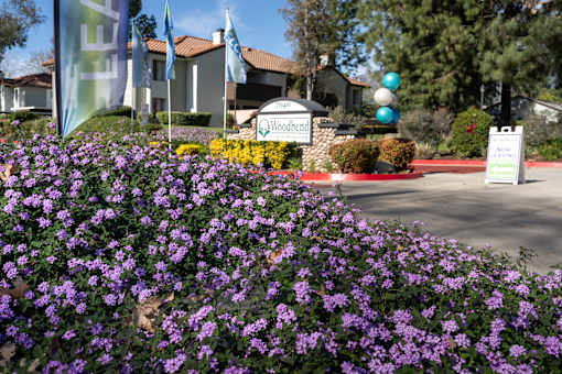 Property entrance sign with purple flowers at Woodbend Apartments, Alta Loma, 91701