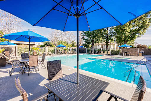 Resort style pool with blue umbrellas and lounge seating at Woodbend Apartments, California
