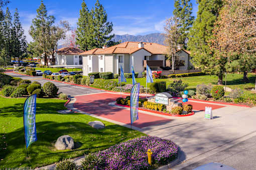 Community entrance with red brick driveway and banners at Woodbend Apartments, Alta Loma