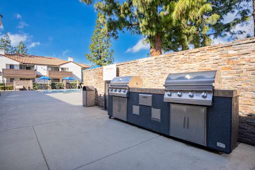 Outdoor barbecue grills with stone accent wall at Woodbend Apartments, Alta Loma, CA 91701