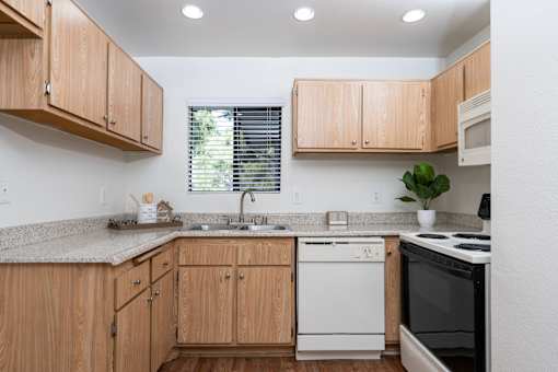 Galley kitchen with wood cabinetry and granite counters at Woodbend Apartments, Alta Loma, CA 91701