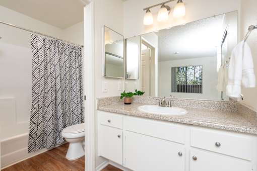 Bathroom with white cabinetry and speckled beige countertop at Woodbend Apartments, California