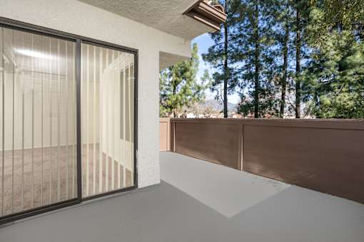 Covered patio with tree views and brown railing at Woodbend Apartments, Alta Loma, California
