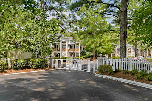A white picket fence surrounds a house with a driveway in front.
