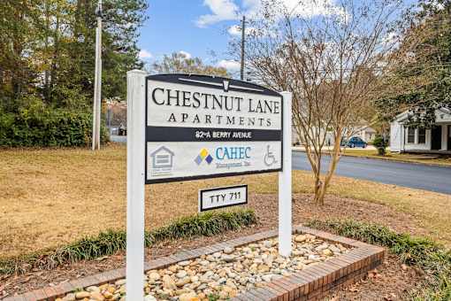 A sign for Chestnut Lane Apartments stands in front of a tree.