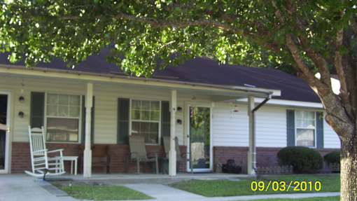 A house with a porch and a tree in front of it.