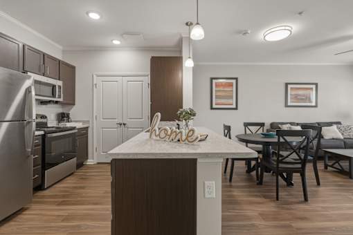 A kitchen with a table and chairs in the foreground and a refrigerator, oven, and microwave in the background.