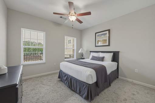 A bedroom with a bed, a ceiling fan, and a window with blinds.
