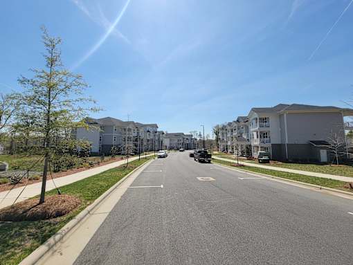 A street view of a residential area with houses on both sides and a car driving down the road.
