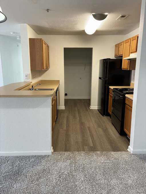 A kitchen with a black refrigerator and wooden cabinets.