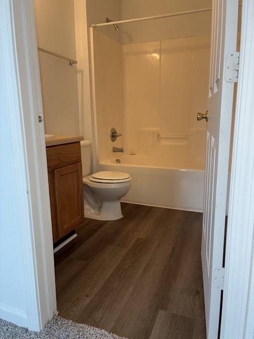 A white toilet is in a bathroom with wood flooring.