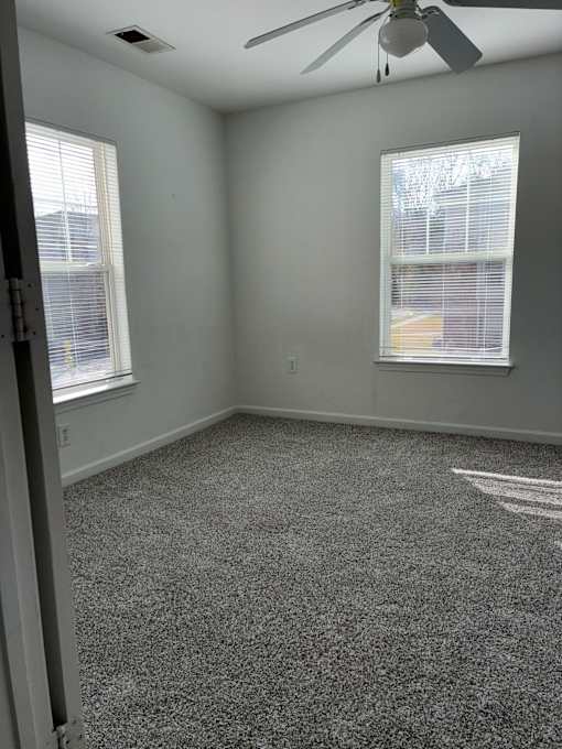 A room with a ceiling fan and two windows.