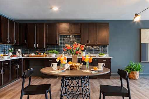 A kitchen with a table set for two with flowers in the middle.