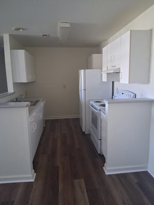 A kitchen with white appliances and wood floors.