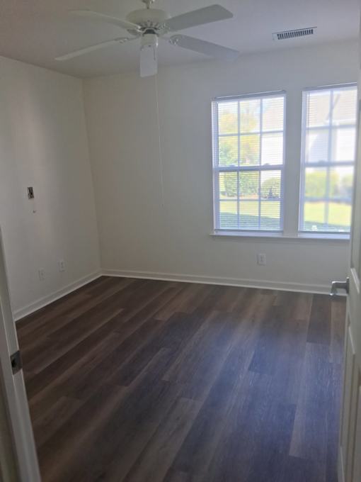 A room with a ceiling fan and two windows.