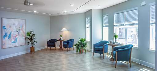 A room with blue chairs and a table with a lamp on it.