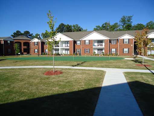 A tree stands in a grassy area in front of apartment buildings.