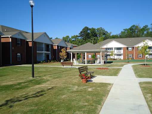 A grassy area with benches and a pathway in front of apartment buildings.