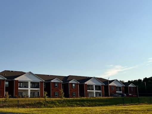 A row of red brick houses with white trim and black fences in front of a grassy field.