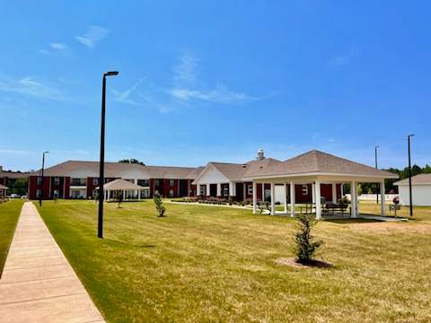 A building with a red roof and white columns is surrounded by a grassy area.