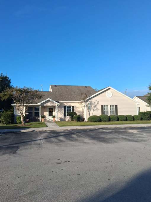 A house with a grey roof and white walls is surrounded by a grassy lawn and a paved driveway.