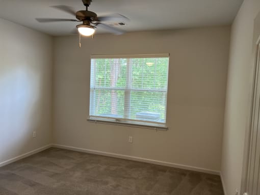 an empty room with a large window and a ceiling fan