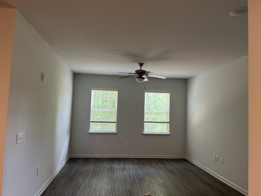 an empty room with a ceiling fan and two windows