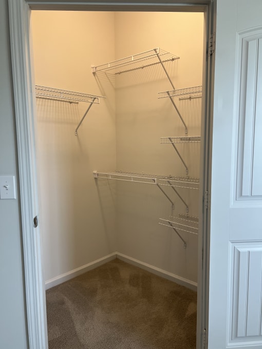 a walk in closet with white walls and a large mirror
