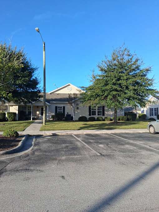 A house with a grey roof and a white front door is surrounded by a parking lot.