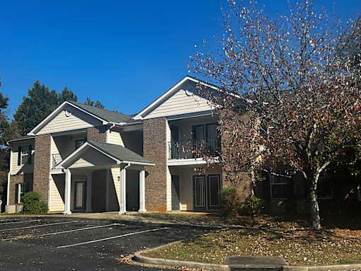 A building with a white and brown facade has a covered walkway leading to the entrance.