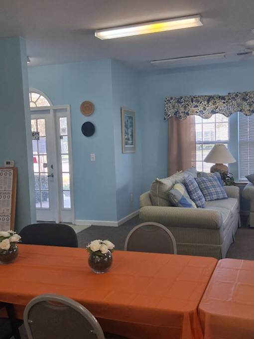 A room with a table set for two with orange tablecloths and a couch with pillows in the background.