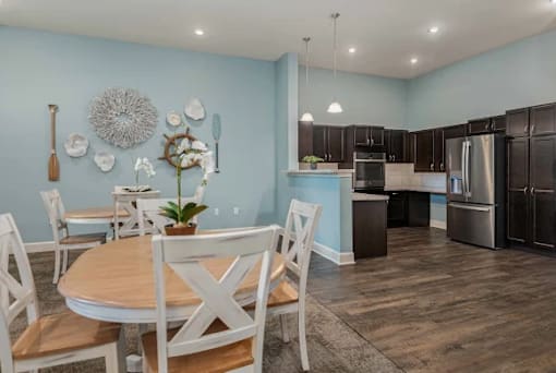 A kitchen with a table and chairs in the foreground and a refrigerator in the background.