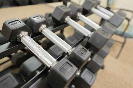 A set of black dumbbells with silver handles are lined up on a wooden surface.