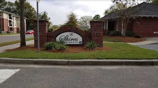 The Shires apartments sign is made of brick and has a green bush in front of it.
