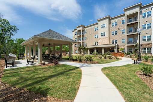 A gazebo is surrounded by a grassy area in front of apartment buildings.