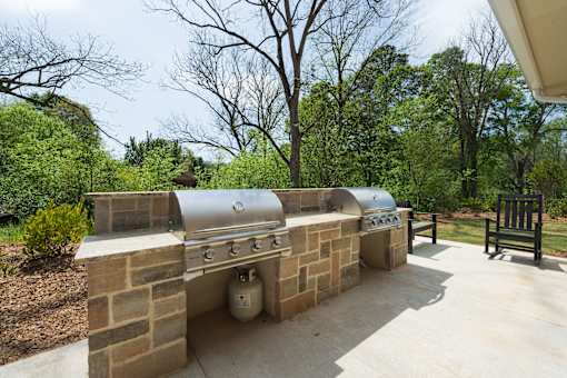 A silver grill is on a patio with a brick wall.