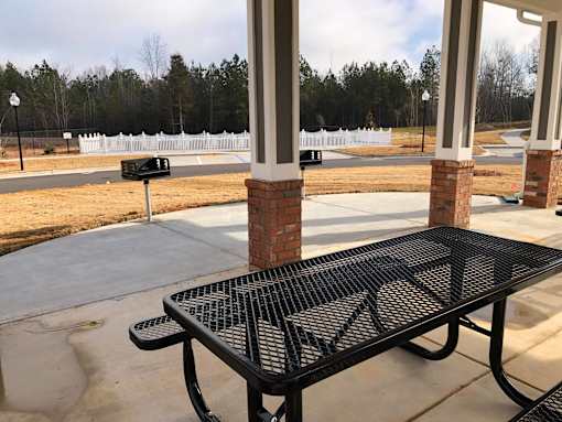 A black metal table is in front of a white fence and a brick pillar.